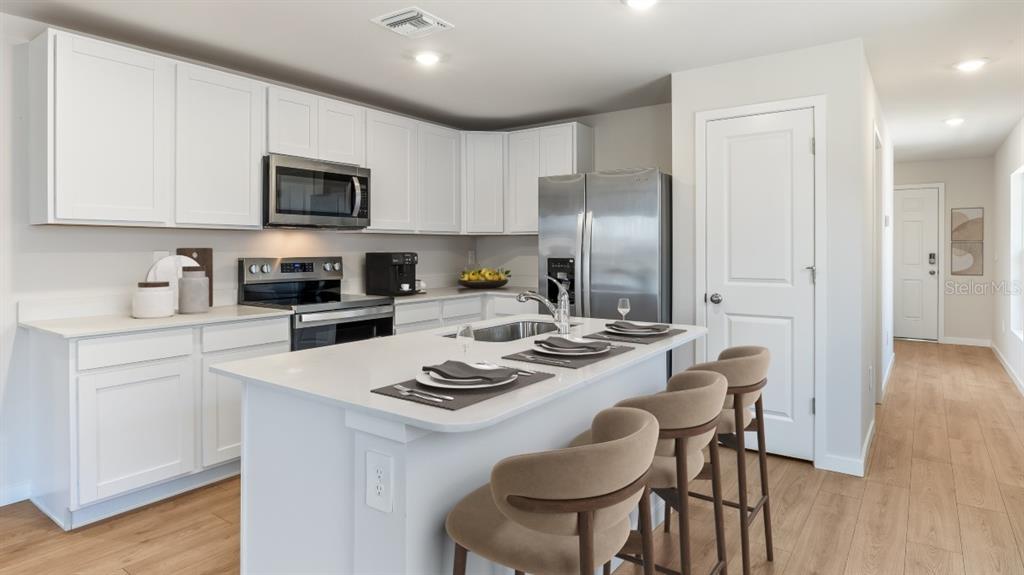 A modern kitchen features white cabinets, stainless steel appliances, a center island, and wood flooring — 26199 SACRED LOTUS LANE, PUNTA GORDA, FL