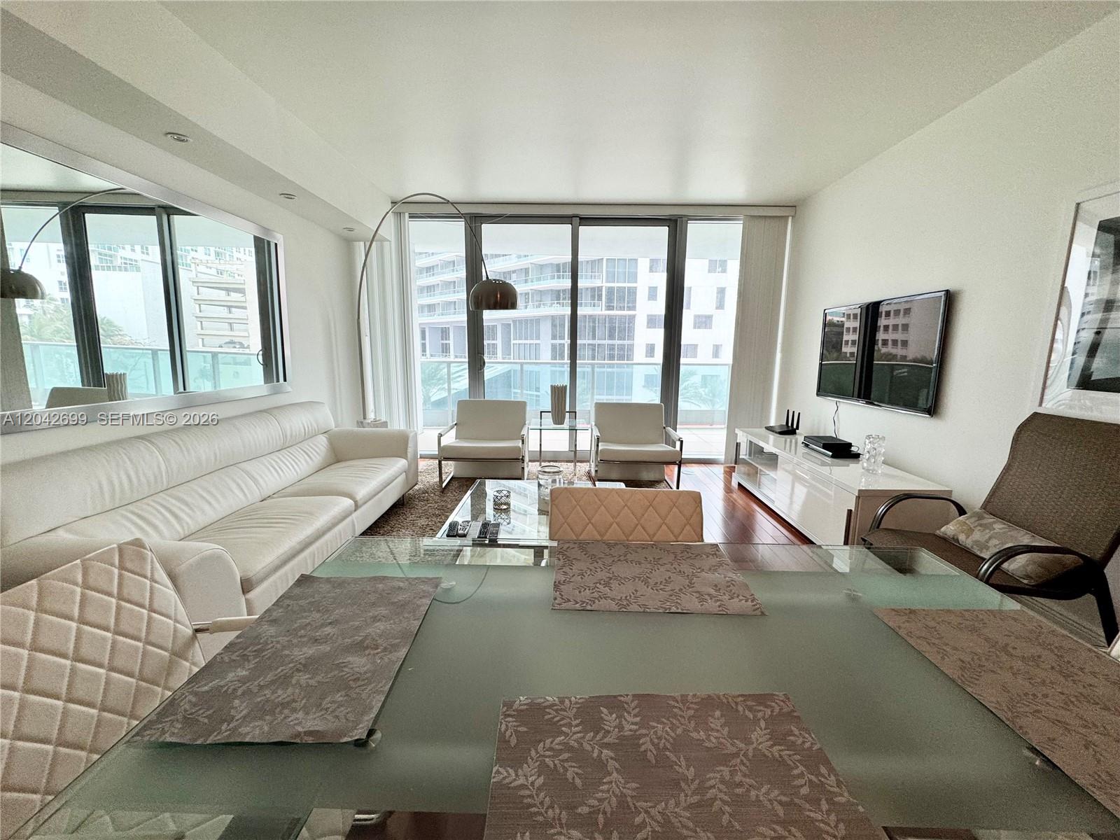 A modern living and dining area features white furniture, a glass table, and balcony views — 1331 Brickell Bay Dr # 406, Miami FL 33131, MIAMI, FL
