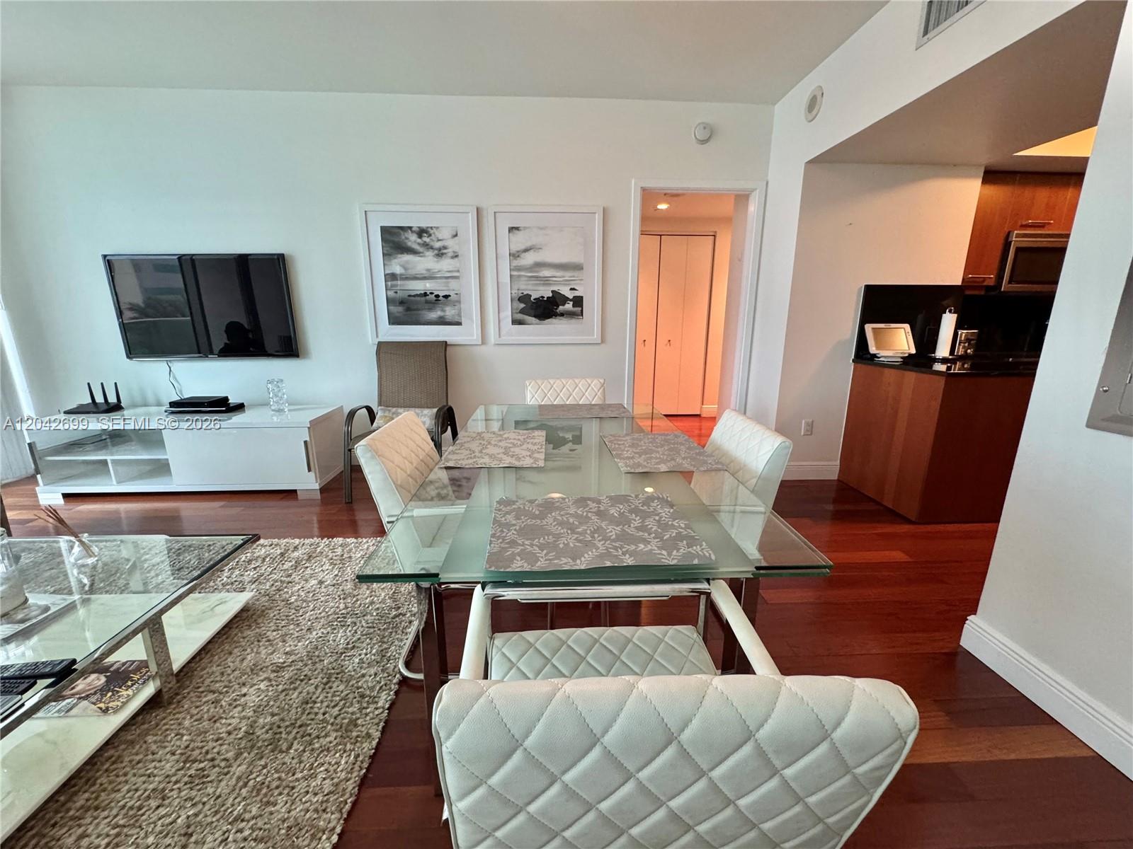 A dining area with a glass table and white chairs sits adjacent to a kitchen — 1331 Brickell Bay Dr # 406, Miami FL 33131, MIAMI, FL
