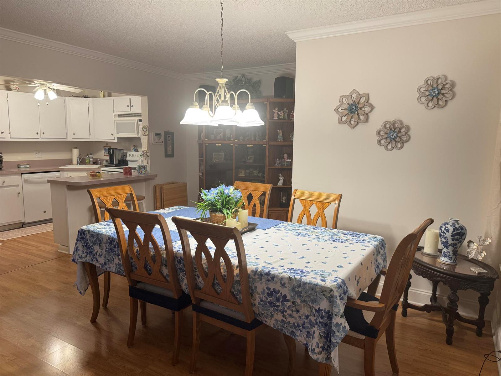A dining room with a floral tablecloth, wooden chairs, and an open view of the kitchen — 417 Pine Glen Lane # 2, FL 33463, FL