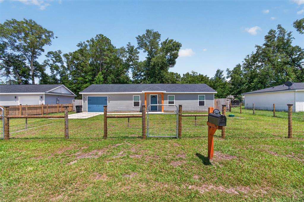 A single-story gray house with a blue garage door sits behind a wire fence — 14027 SE 43RD TERRACE, SUMMERFIELD, FL