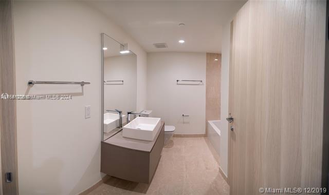 A modern bathroom features a floating vanity with a white sink, mirror, and bathtub — 1000 Brickell Plz # 4905, Miami FL 33131, MIAMI, FL