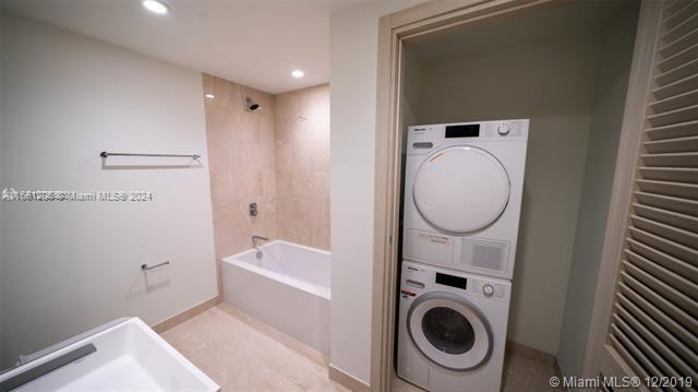 A bathroom features a white bathtub, a stacked washer and dryer, and light-colored tile walls — 1000 Brickell Plz # 4905, Miami FL 33131, MIAMI, FL