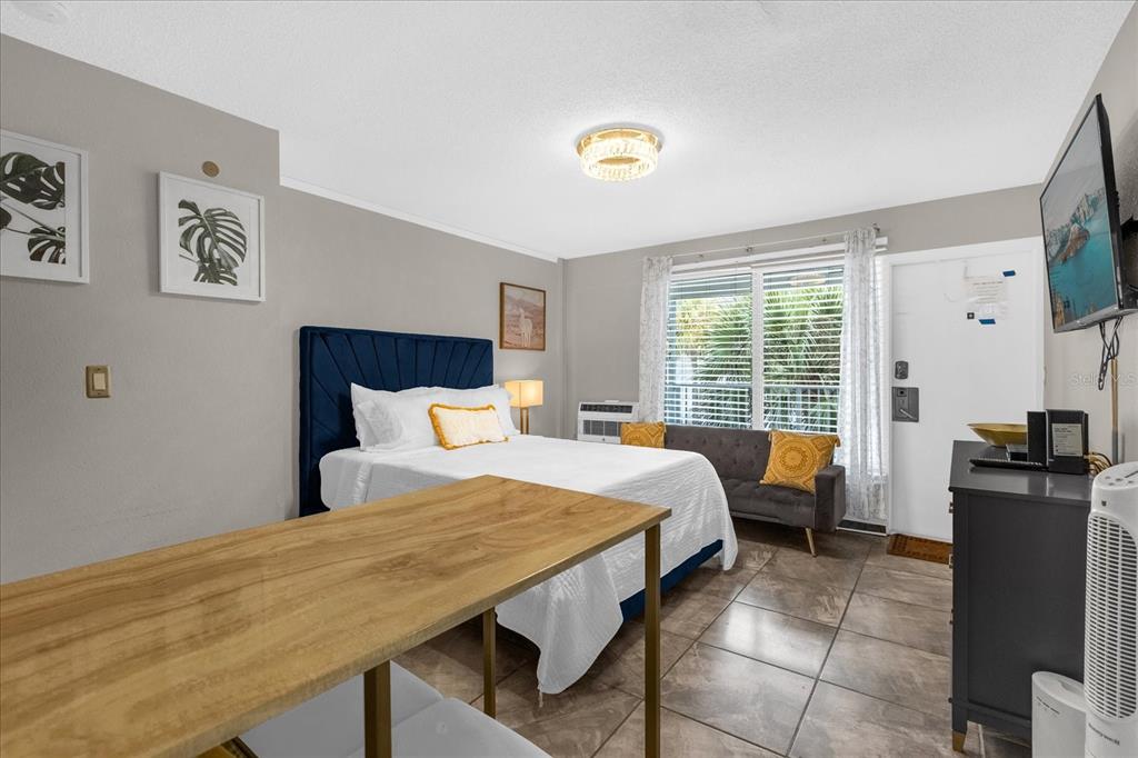 A bedroom features a blue tufted headboard, a wooden table, and a gray sofa — 935 S ATLANTIC AVENUE UNIT 239, DAYTONA BEACH, FL