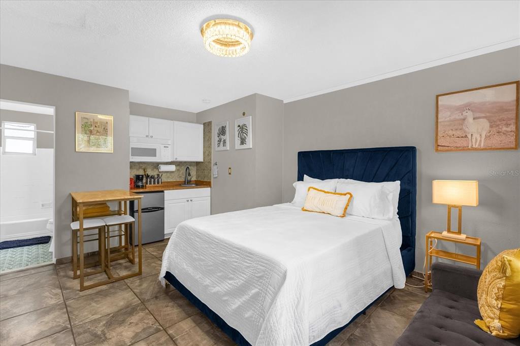A studio apartment features a kitchenette, a queen bed with a blue headboard, and tile flooring — 935 S ATLANTIC AVENUE UNIT 239, DAYTONA BEACH, FL