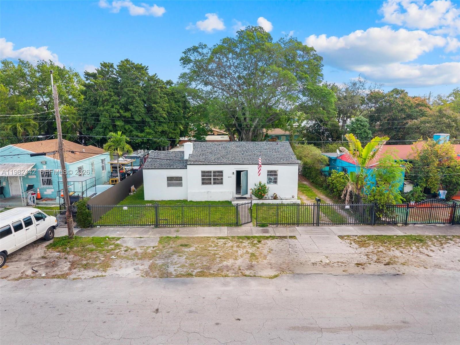 A white single-story house with a gray roof sits behind a black metal fence — 6223 NW Miami Pl, Miami FL 33150, MIAMI, FL