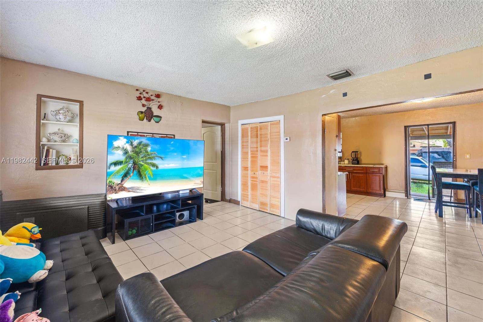 A living room features tile flooring, a black leather sofa, and a television on a stand — 6223 NW Miami Pl, Miami FL 33150, MIAMI, FL