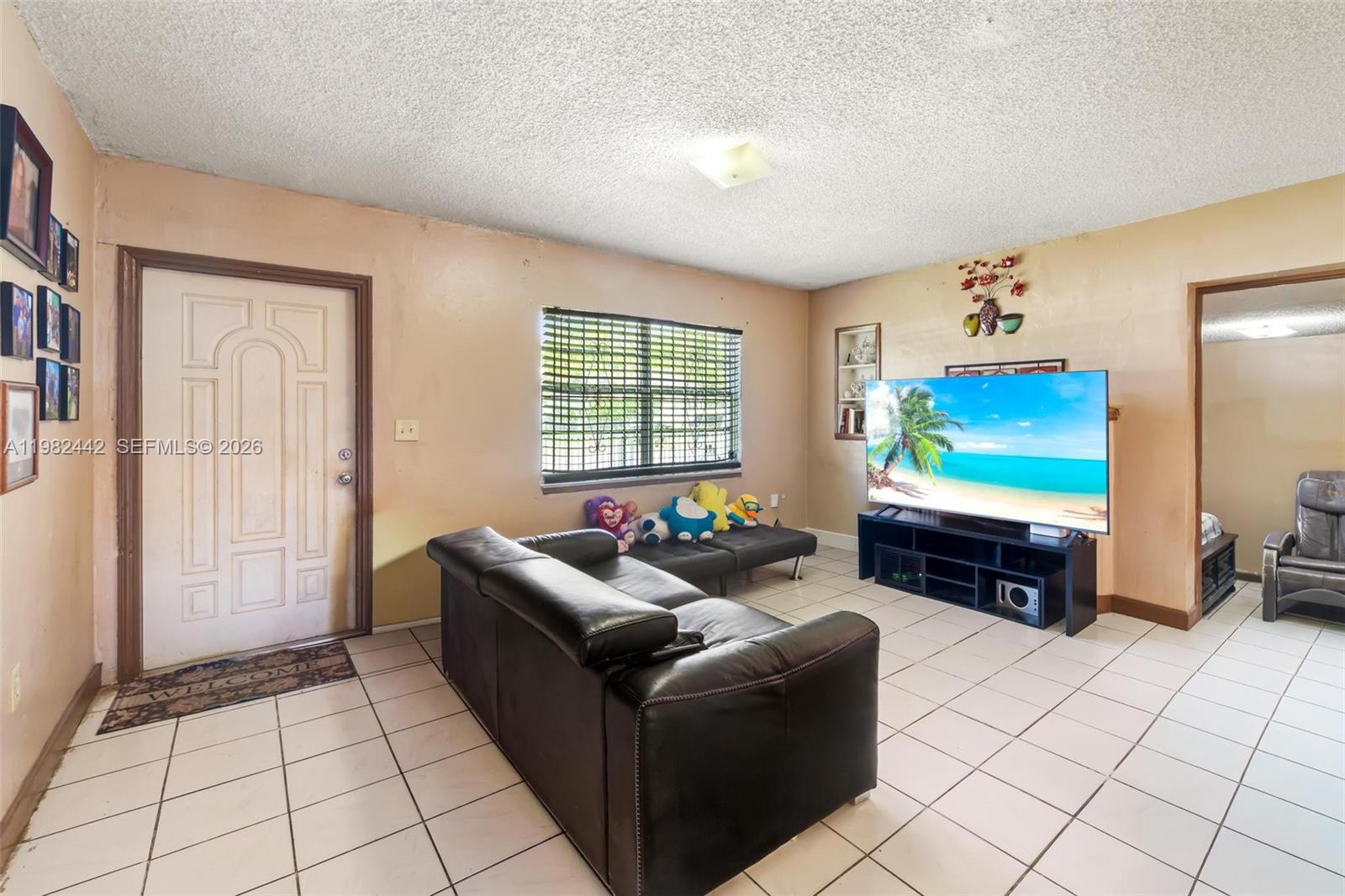 A living room features a black leather sofa, a large television, and white tile flooring — 6223 NW Miami Pl, Miami FL 33150, MIAMI, FL