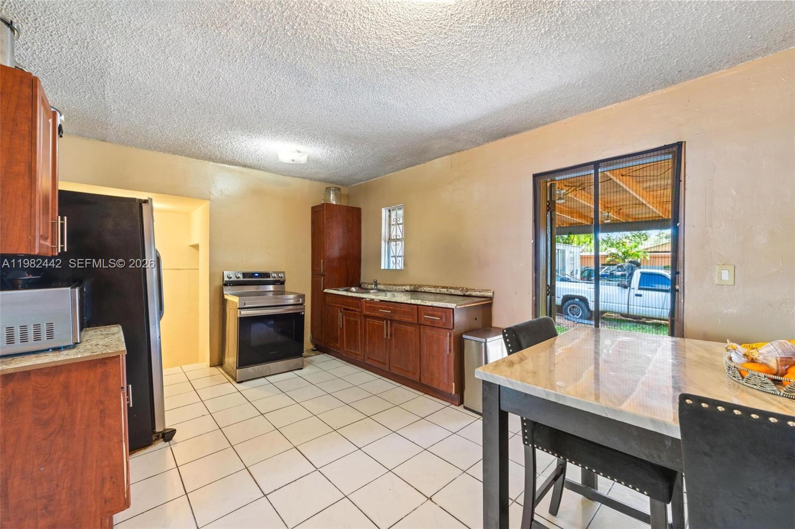 A kitchen features wood cabinets, stainless steel appliances, tile flooring, and a sliding glass door — 6223 NW Miami Pl, Miami FL 33150, MIAMI, FL