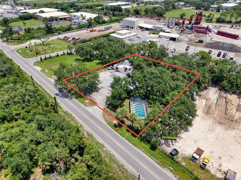 An aerial view shows a house with a screened pool surrounded by trees and industrial lots — 4727 15TH STREET E, BRADENTON, FL
