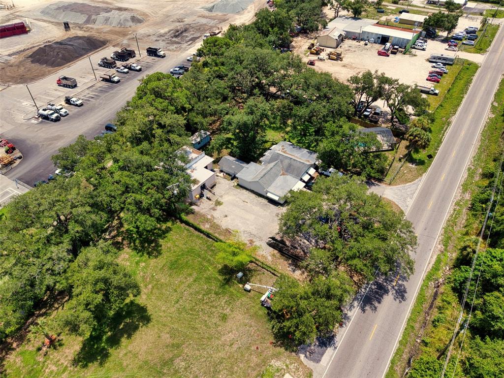 An aerial view shows a house and a commercial building surrounded by trees and pavement — 4727 15TH STREET E, BRADENTON, FL