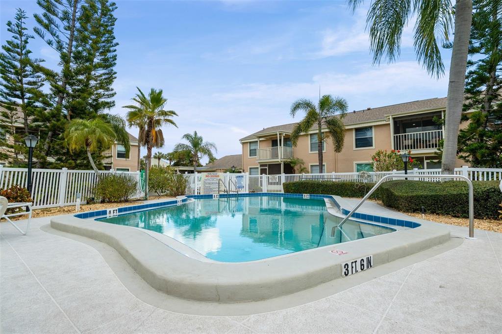 An outdoor swimming pool is surrounded by a white fence and multi-story apartment buildings — 6320 7TH AVENUE W, BRADENTON, FL