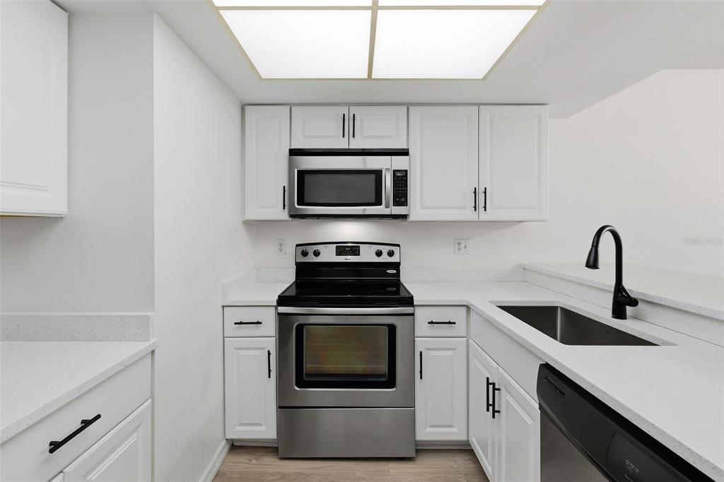 A galley kitchen features white cabinets, stainless steel appliances, and light-colored countertops — 6320 7TH AVENUE W, BRADENTON, FL