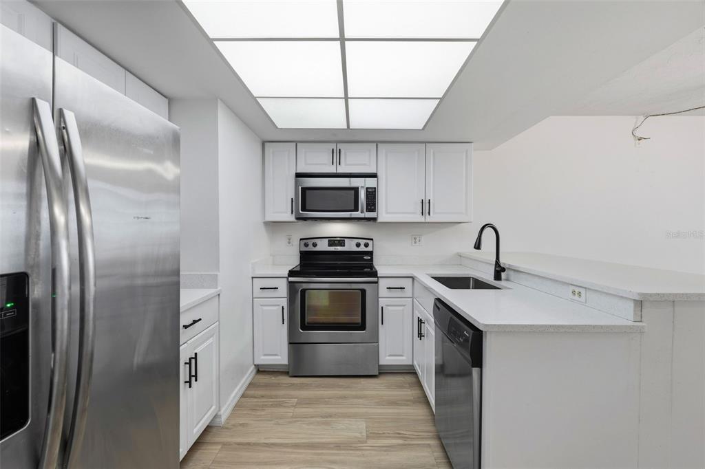 A living and kitchen area with wood-look flooring, white cabinets, and two ceiling fans — 6320 7TH AVENUE W, BRADENTON, FL