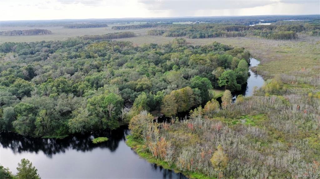 An aerial view shows a winding river flowing through a dense forest and marshland — 10909 E FLOUNDER DRIVE, FLORAL CITY, FL