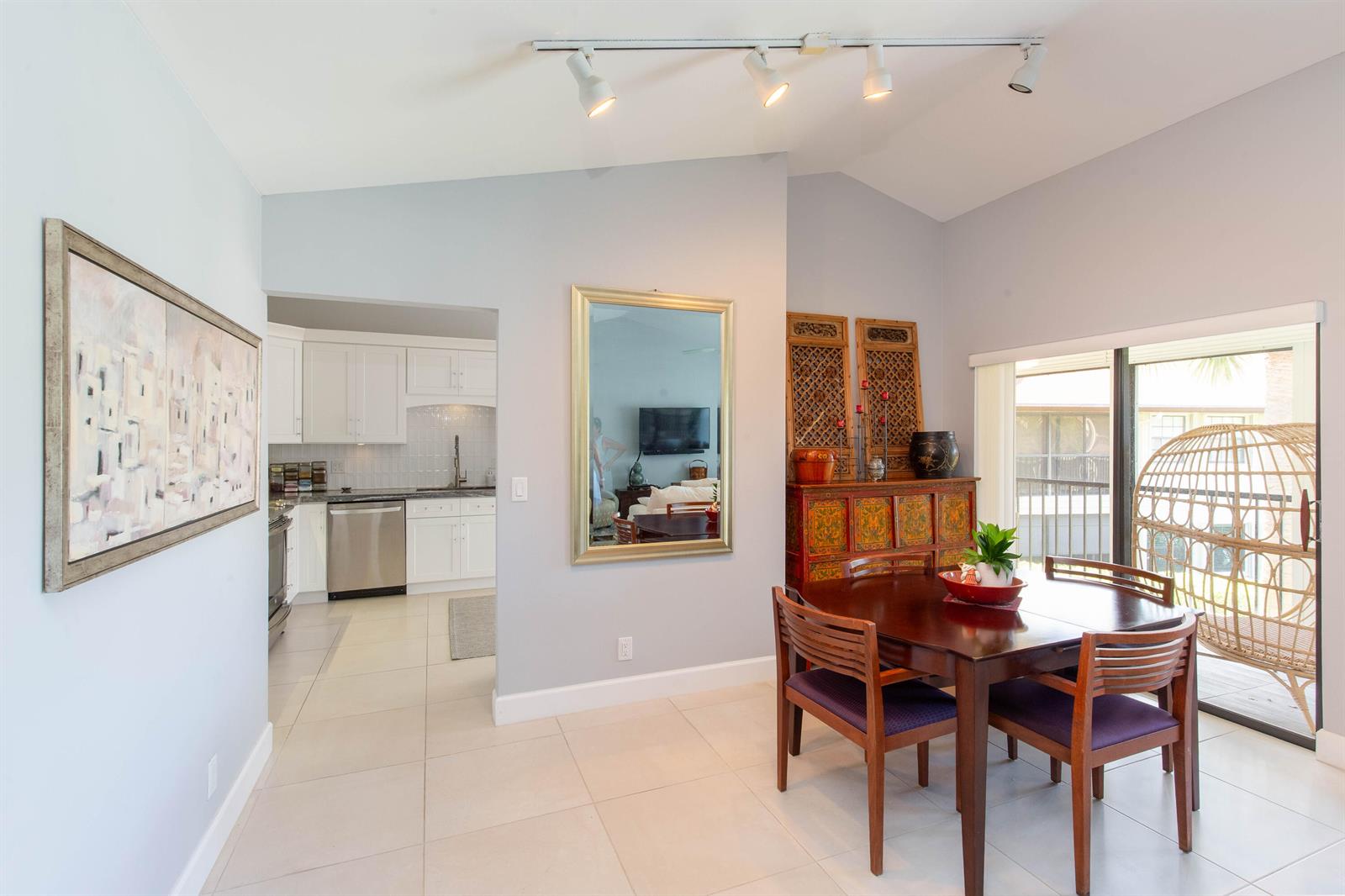 A dining area with a wooden table, chairs, a mirror, and an adjacent white kitchen — 3399 Jog Park Drive, FL 33467, FL