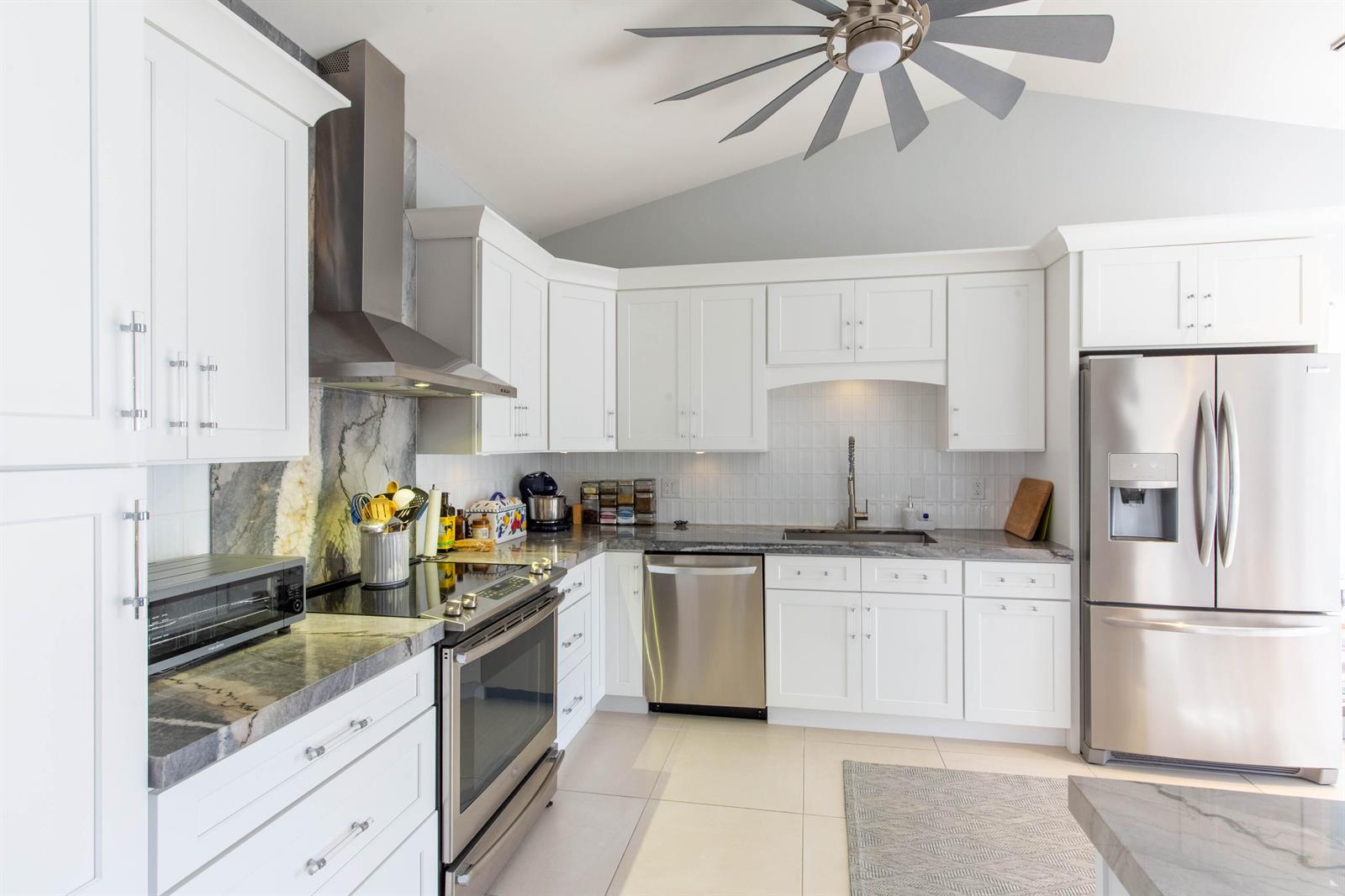 A modern kitchen features white cabinetry, stainless steel appliances, and gray stone countertops — 3399 Jog Park Drive, FL 33467, FL