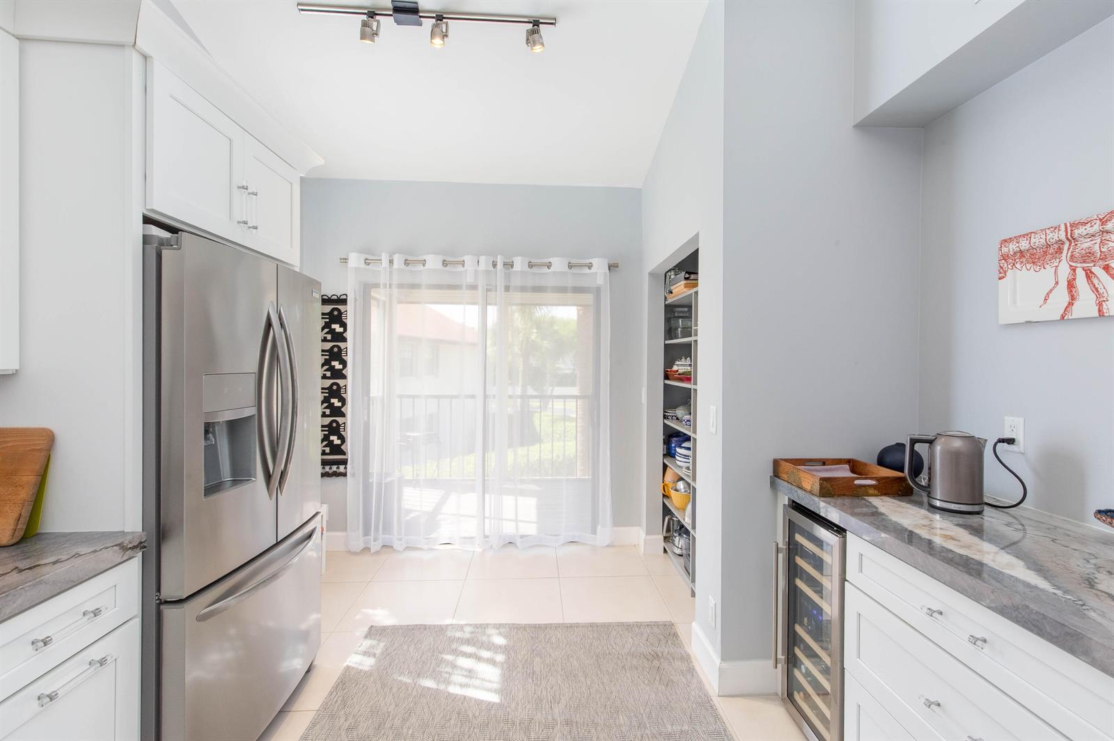 A kitchen features a stainless steel refrigerator, wine cooler, white cabinetry, and a sliding glass door — 3399 Jog Park Drive, FL 33467, FL