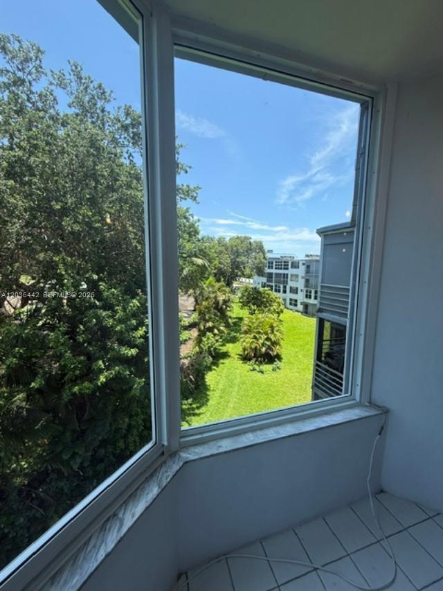 A view of a grassy courtyard and neighboring buildings from a tiled indoor balcony — 1101 NE 191st St # H401, Miami FL 33179, MIAMI, FL