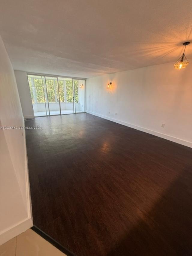 An empty living room features dark wood flooring, white walls, and a glass-enclosed balcony — 1101 NE 191st St # H401, Miami FL 33179, MIAMI, FL