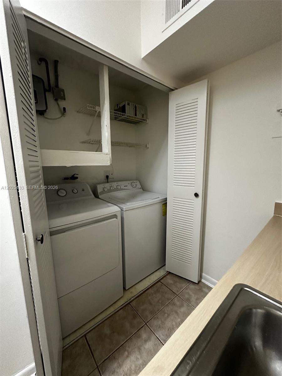 A laundry closet contains a washer and dryer beneath wire shelving and a circuit breaker — 18356 NW 68th Ave # K, Hialeah FL 33015, HIALEAH, FL