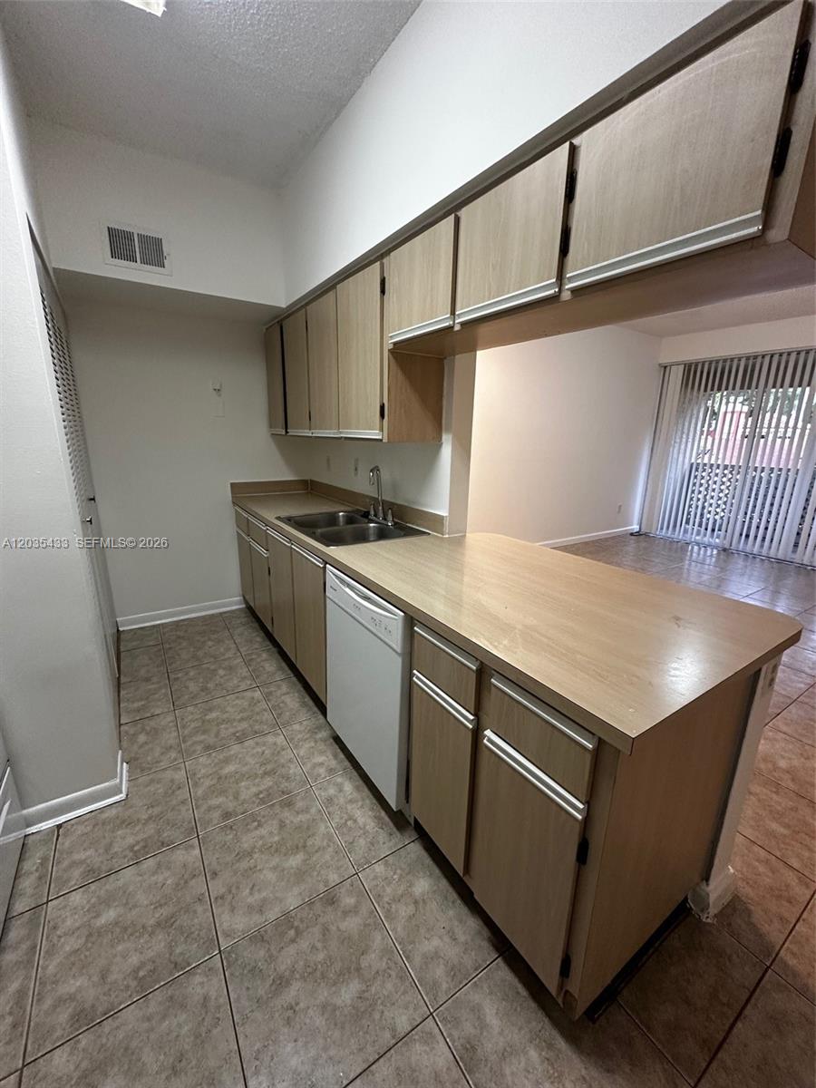 A kitchen features light wood cabinets, a white dishwasher, and tan tile flooring — 18356 NW 68th Ave # K, Hialeah FL 33015, HIALEAH, FL