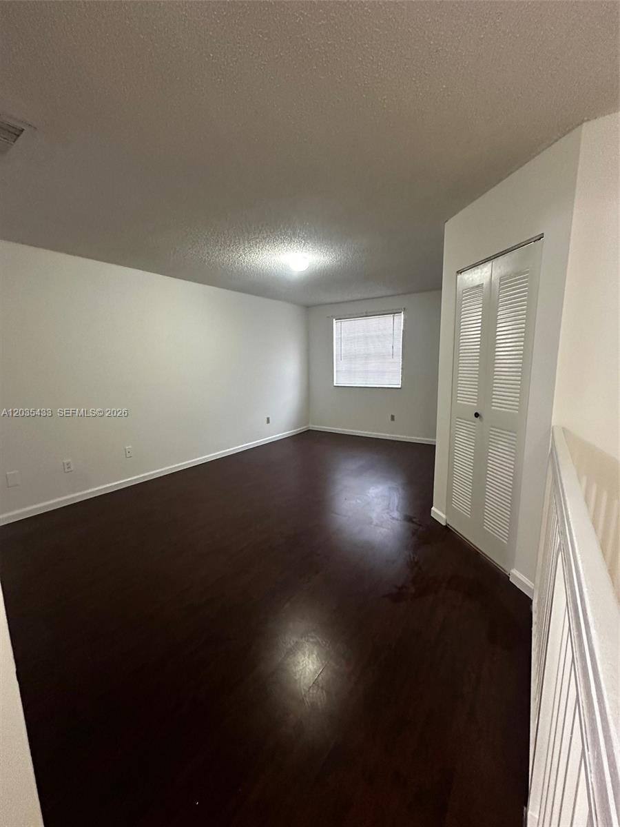 An empty room features dark wood flooring, white walls, a window, and a closet — 18356 NW 68th Ave # K, Hialeah FL 33015, HIALEAH, FL