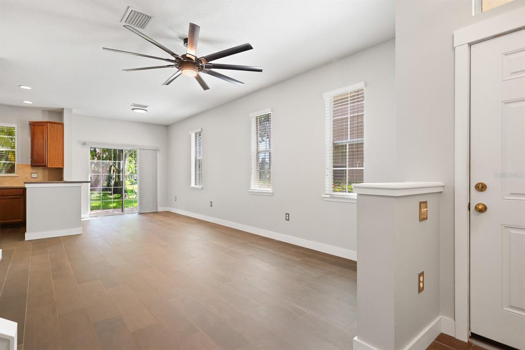 A bright living room features light wood-look flooring, a ceiling fan, and three large windows — 9133 MOONLIT MEADOWS LOOP, RIVERVIEW, FL