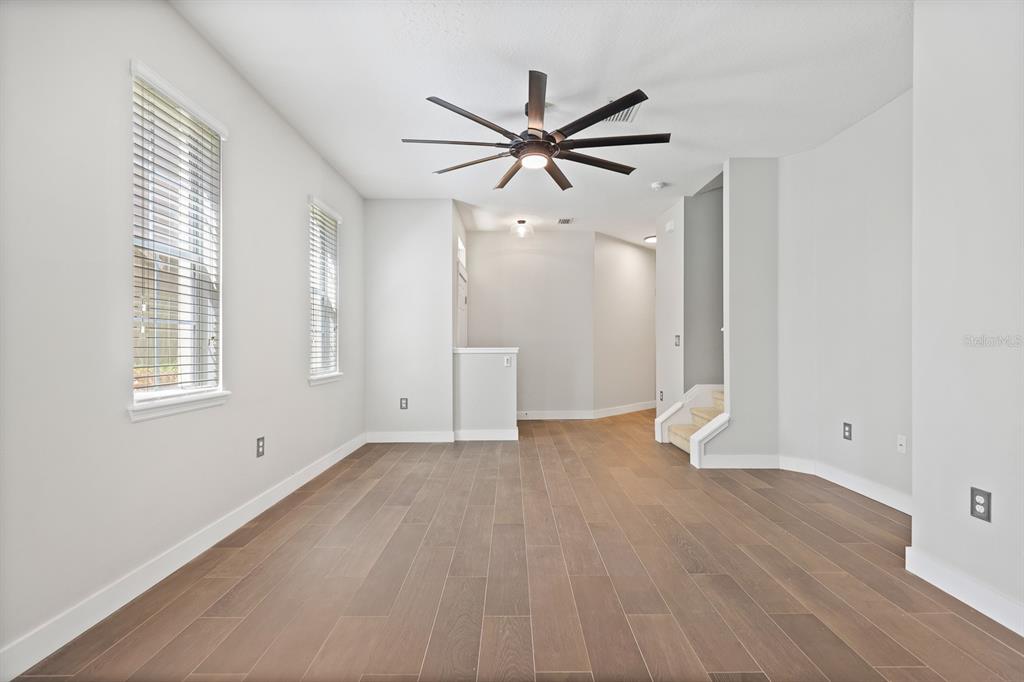 An empty room with wood-look flooring, white walls, a ceiling fan, and a staircase — 9133 MOONLIT MEADOWS LOOP, RIVERVIEW, FL