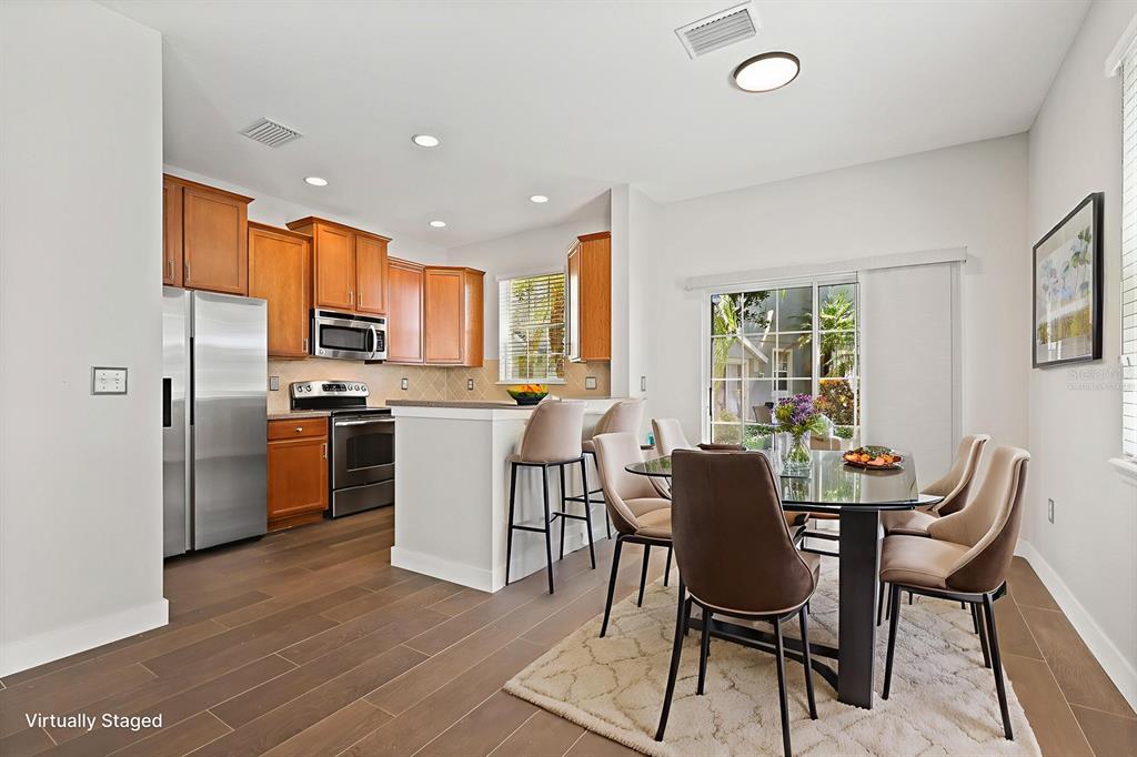 A kitchen with wood cabinets and stainless appliances opens to a dining area with sliding doors — 9133 MOONLIT MEADOWS LOOP, RIVERVIEW, FL