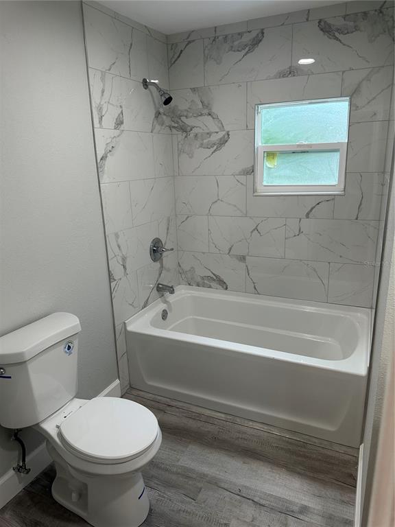 A bathroom features a white toilet, a bathtub with marble-look tile walls, and wood-look flooring — 507 STONE STREET, WILDWOOD, FL