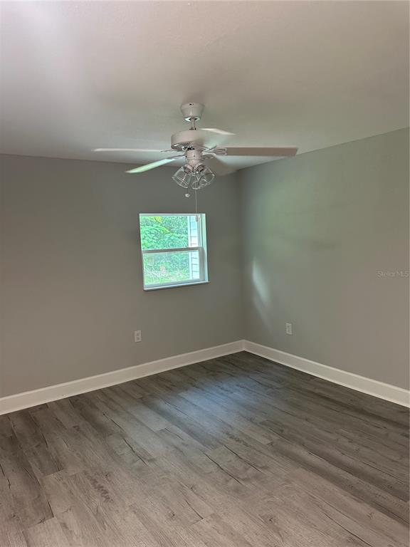 An empty bedroom with gray walls, white trim, and wood-look flooring under a ceiling fan — 507 STONE STREET, WILDWOOD, FL
