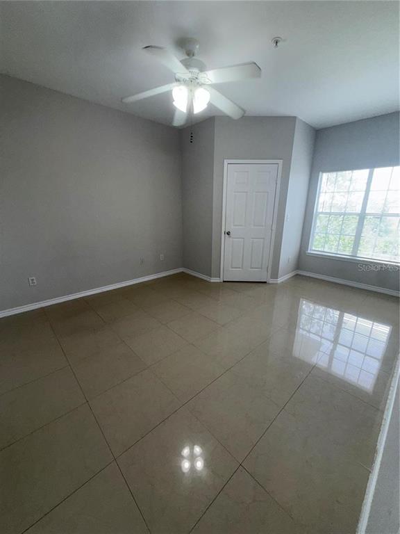 An empty room with light-colored tile flooring, gray walls, a ceiling fan, and a window — 4304 BAYSIDE VILLAGE DRIVE UNIT 303, TAMPA, FL