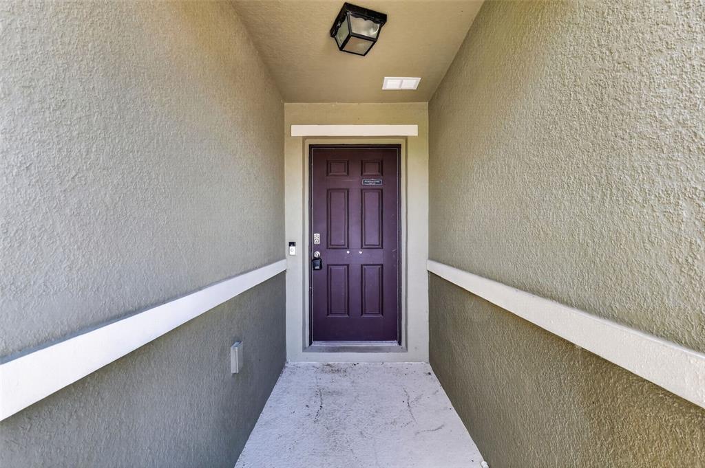 A dark purple front door is centered at the end of a covered entryway — 2465 BEGONIA STREET, MASCOTTE, FL