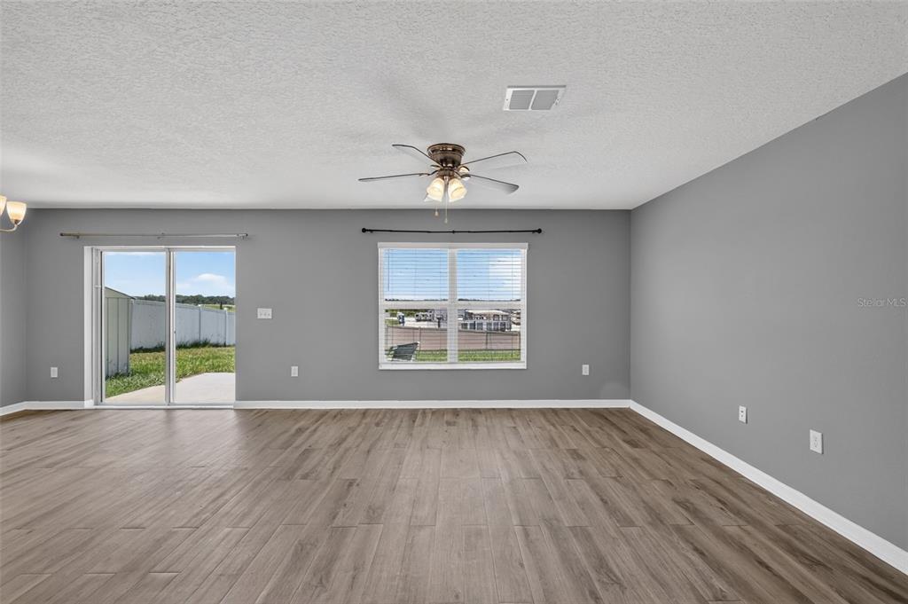 An empty living room features gray walls, wood-look flooring, a ceiling fan, and sliding doors — 2465 BEGONIA STREET, MASCOTTE, FL