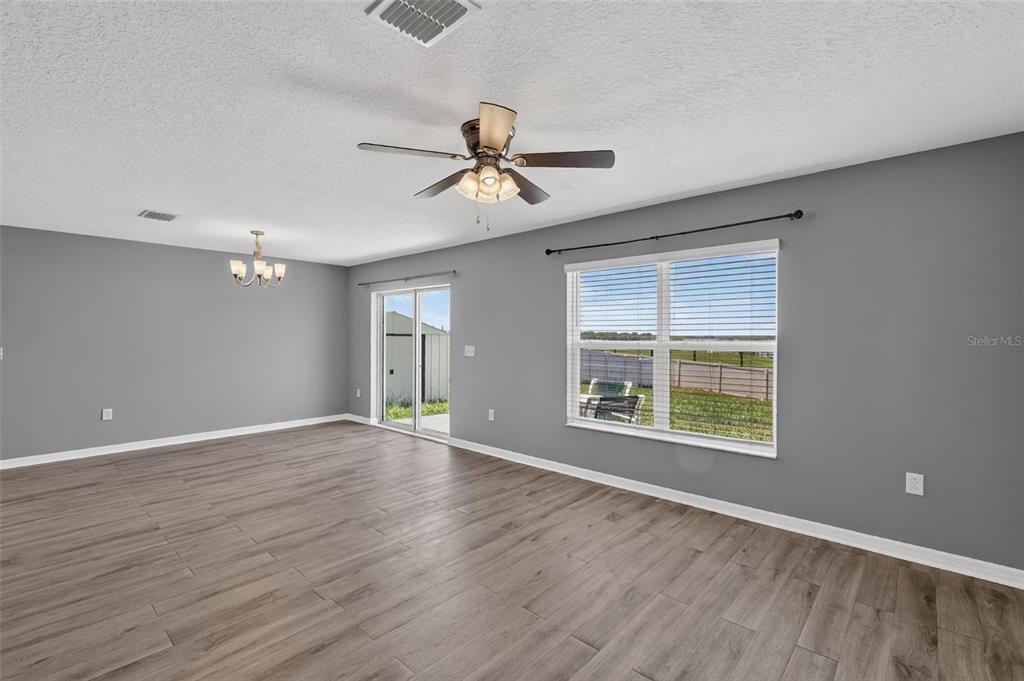 A living room with gray walls, wood-look flooring, a ceiling fan, and a sliding door — 2465 BEGONIA STREET, MASCOTTE, FL