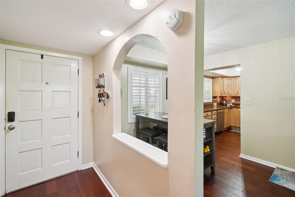 An entryway with a white door, arched wall cutout, and hardwood floors leading to a kitchen — 8300 BARDMOOR BOULEVARD UNIT 103, SEMINOLE, FL
