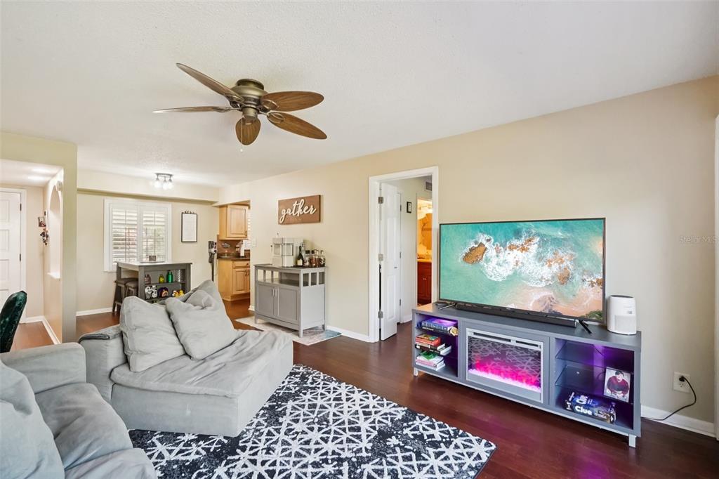 A living room with a gray sectional, patterned rug, media console, and an open kitchen — 8300 BARDMOOR BOULEVARD UNIT 103, SEMINOLE, FL