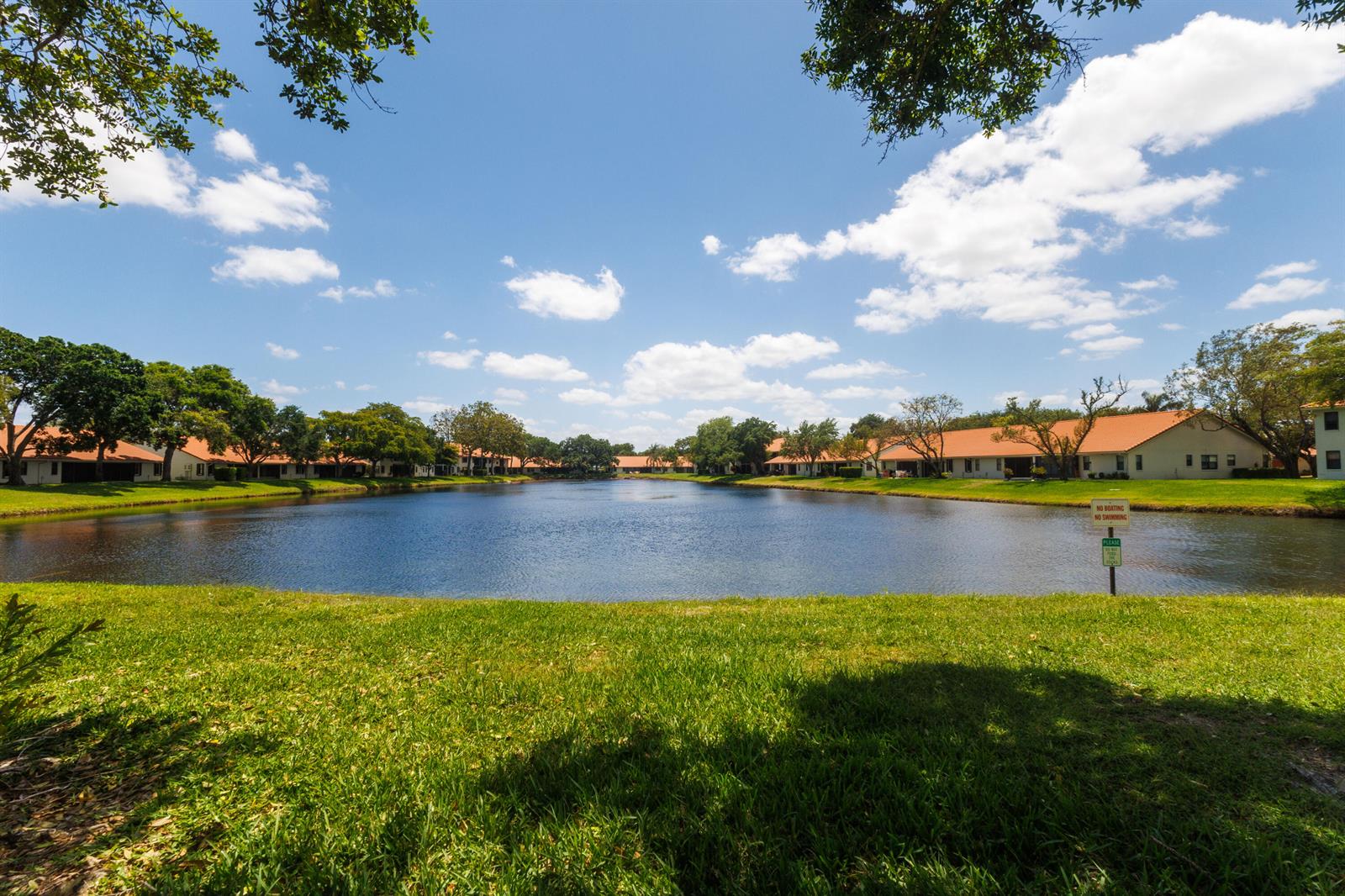 A view of a pond surrounded by residential buildings and green lawns under a blue sky — 9700 Pavarotti Terrace # 102, Boynton Beach FL 33437, BOYNTON BEACH, FL