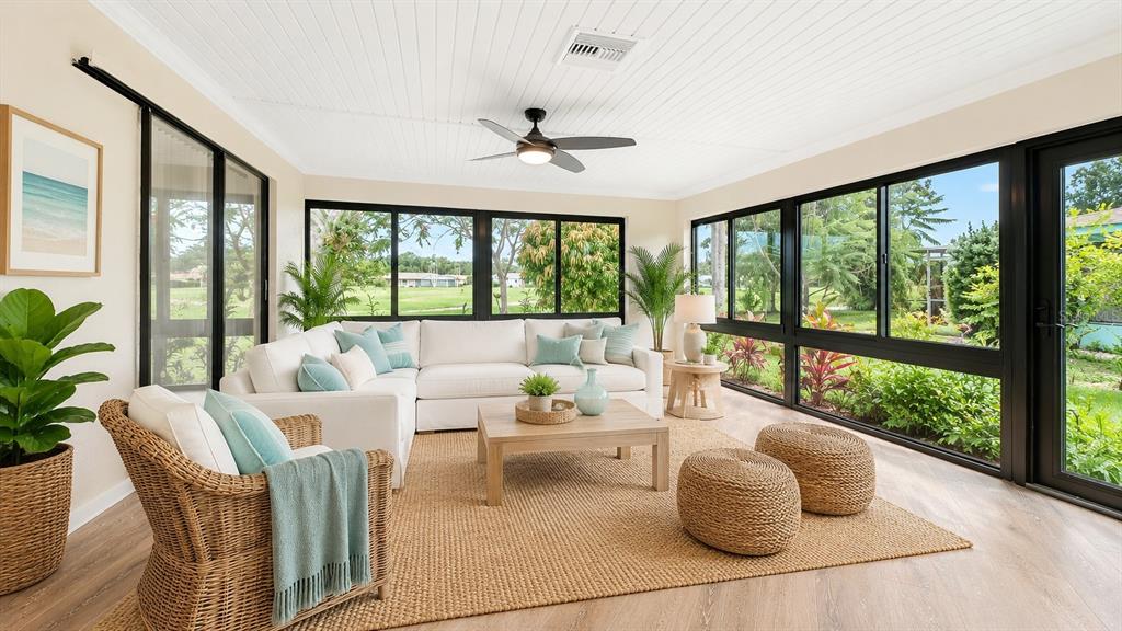 A sunroom features a white sectional sofa, wicker armchair, jute rug, and large black-framed windows — 4777 RINGWOOD MEADOW, SARASOTA, FL