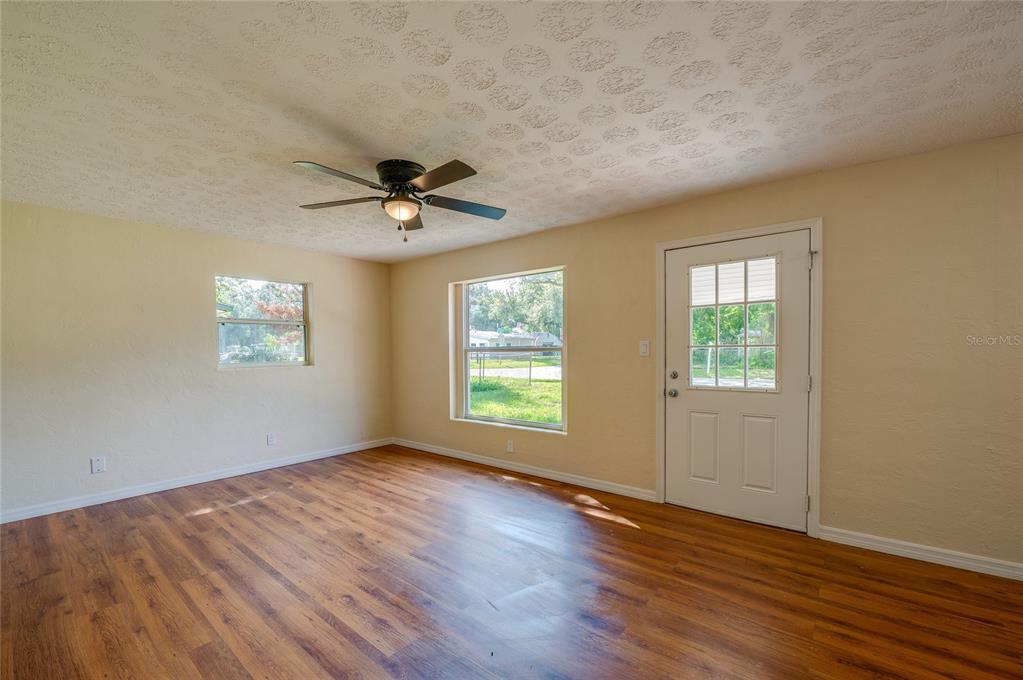 An empty room features light-colored walls, wood-look flooring, a ceiling fan, and two windows — 1220 LEON LANE, DAYTONA BEACH, FL