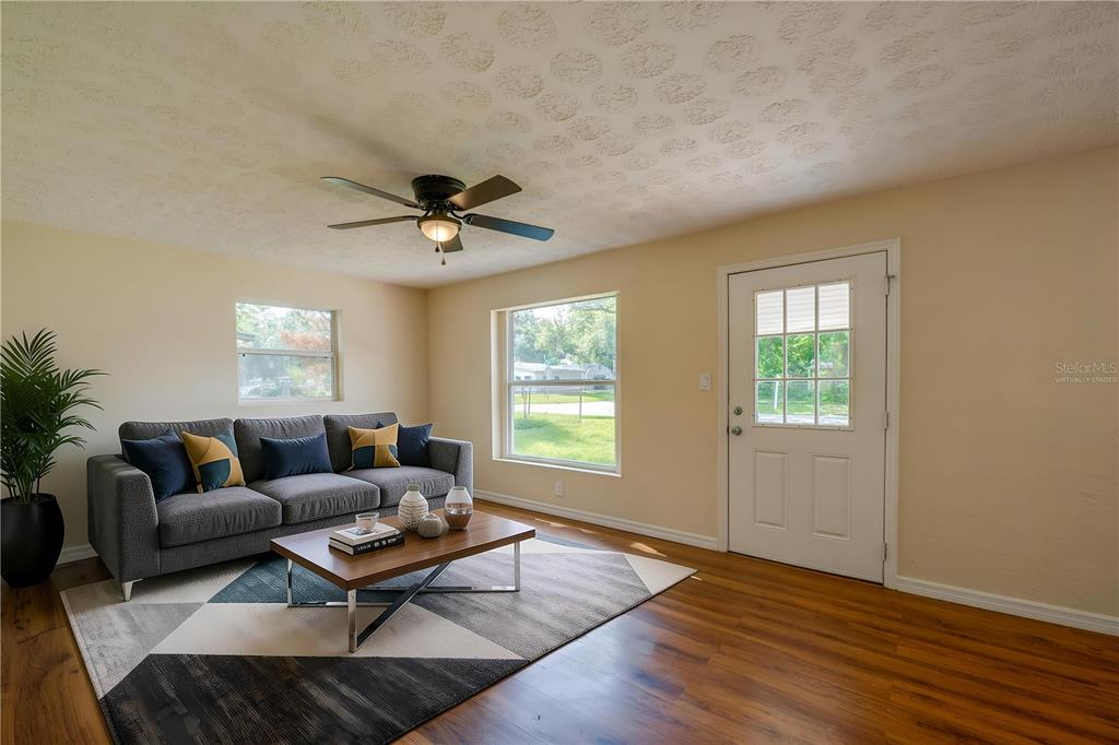 A living room features a gray sofa, wood floors, a ceiling fan, and two windows — 1220 LEON LANE, DAYTONA BEACH, FL