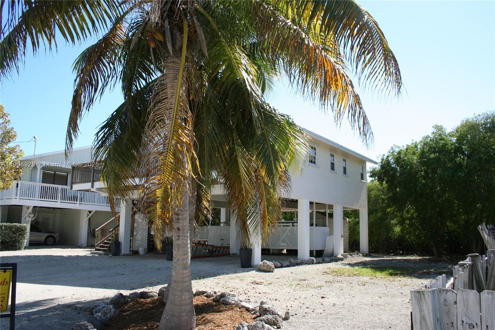 A stilt house with a gravel driveway and a large palm tree in the foreground — 150 Peace Ave, Key Largo FL 33037, KEY LARGO, FL