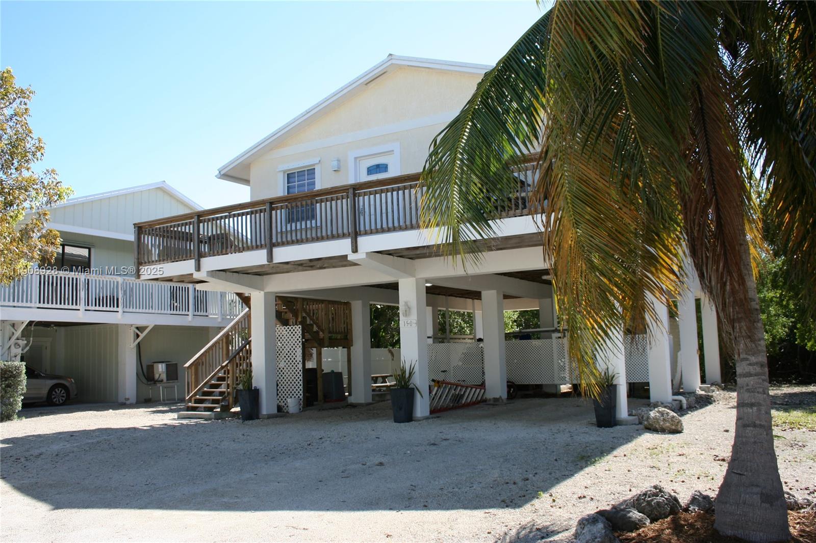 An elevated house with a wooden deck and staircase stands over a gravel driveway — 150 Peace Ave, Key Largo FL 33037, KEY LARGO, FL