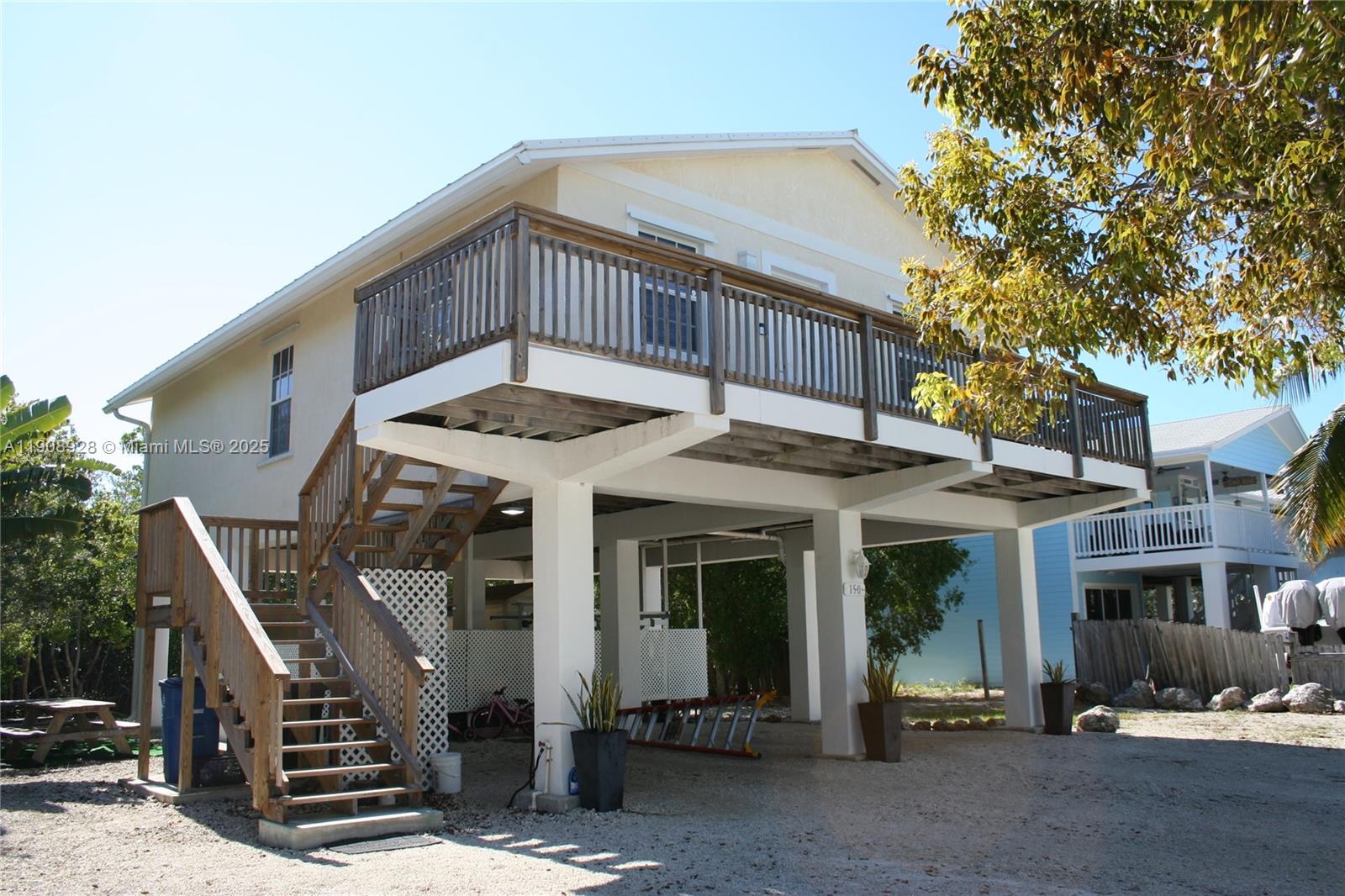 An elevated house with a wooden deck, outdoor staircase, and covered parking area underneath — 150 Peace Ave, Key Largo FL 33037, KEY LARGO, FL