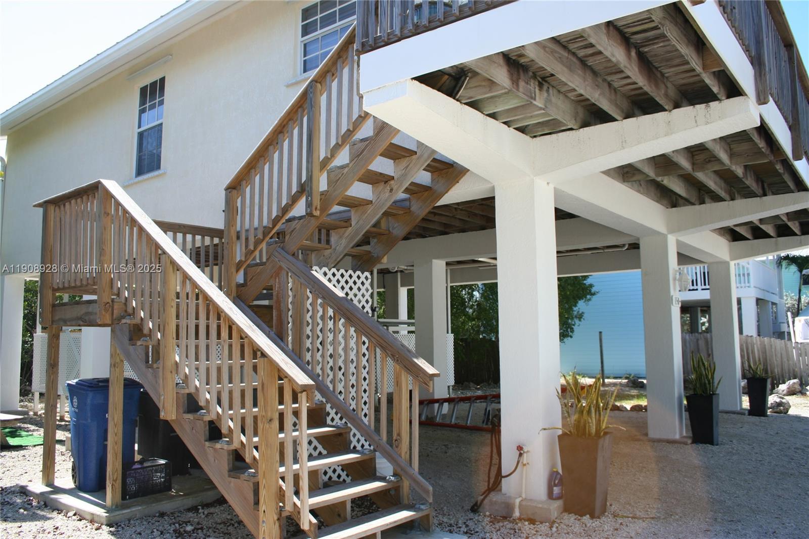 An exterior view of a stilt house featuring a wooden staircase leading to an elevated deck — 150 Peace Ave, Key Largo FL 33037, KEY LARGO, FL
