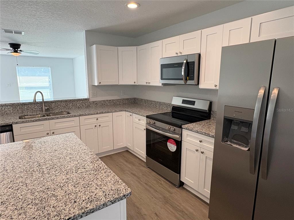 A kitchen features white cabinets, granite countertops, stainless steel appliances, and light wood-look flooring — 319 PEARL STREET, LAKE WALES, FL
