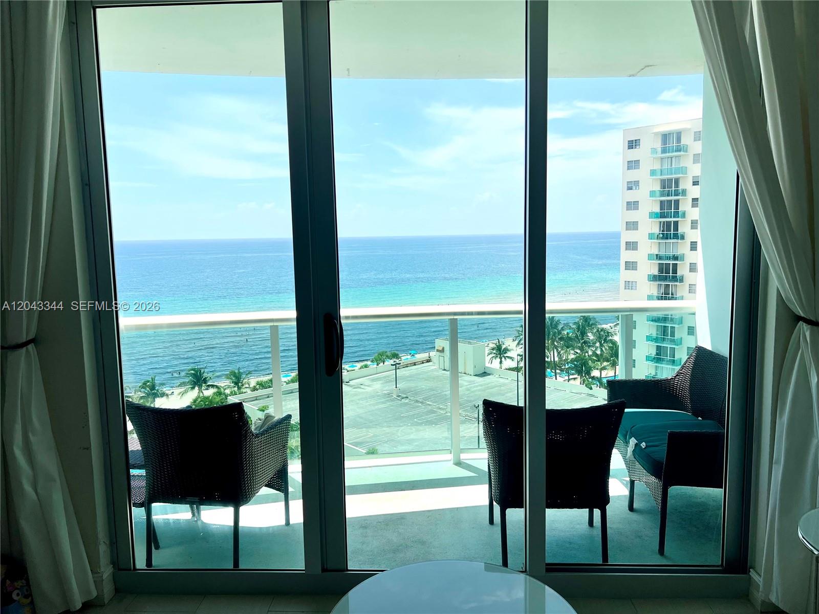 A balcony with outdoor seating overlooks the ocean and a neighboring high-rise building — 3801 S Ocean Dr # 11M, Hollywood FL 33019, HOLLYWOOD, FL