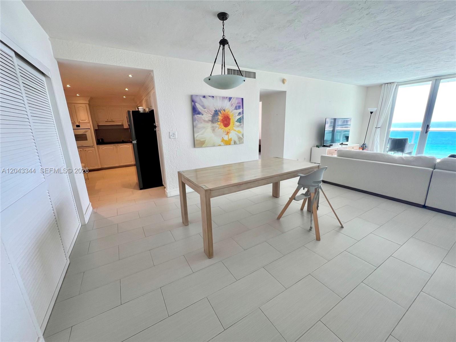 A dining area features a wooden table, a high chair, and a view of the ocean — 3801 S Ocean Dr # 11M, Hollywood FL 33019, HOLLYWOOD, FL