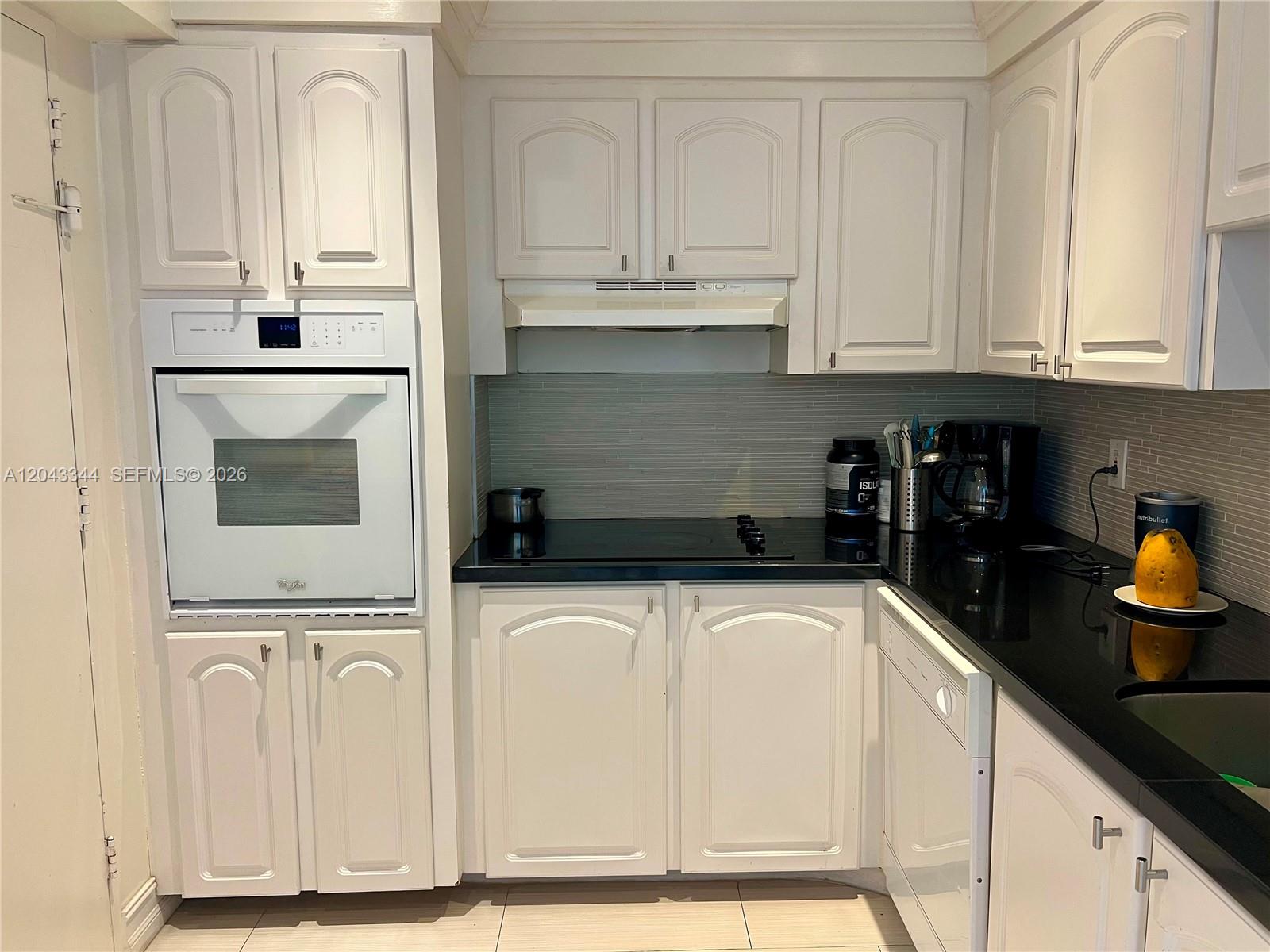 A kitchen features white cabinets, black countertops, a wall oven, and a glass cooktop — 3801 S Ocean Dr # 11M, Hollywood FL 33019, HOLLYWOOD, FL